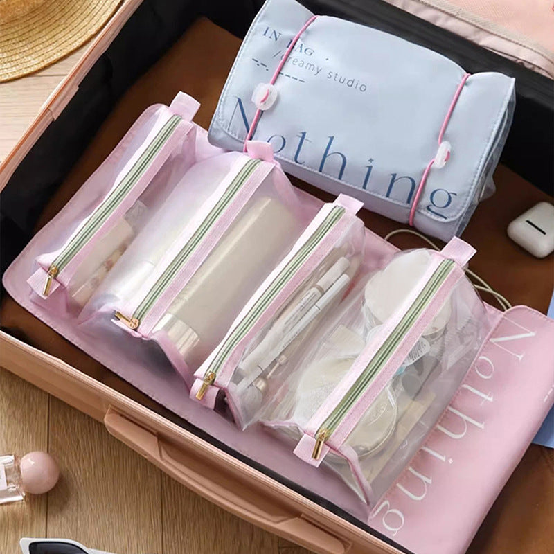 Roze uitvouwbare toilettas met vier transparante ritsvakken voor verzorgingsproducten, geopend in een koffer.